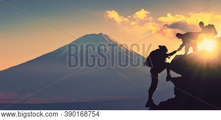 Young Asian Couple Hikers Climbing Up On The Peak Of Mountain Near Mountain Fuji. People Helping Eac