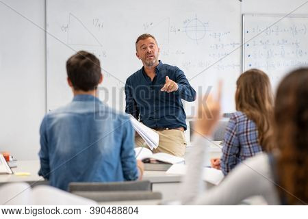 Professor pointing at college student with hand raised in classroom. Student raising a hand with a question for the teacher. Lecturer teaching in class while girl have a question to do during a lesson