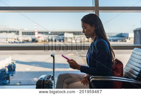 Airport phone travel woman using mobile phone in business class lounge waiting for plane flight texting sms message on smartphone. Technology and travel people frequent flying lifestyle.