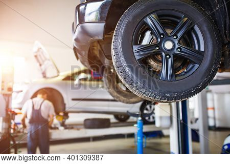 The Car Is Lifted For Repair On A Lift In A Car Service Station, A Mechanic In Overalls Repairs In T