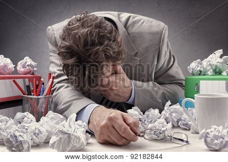 Overworked, depressed and exhausted businessman at his desk with a pile of work or concept for frustration, stress and writers block