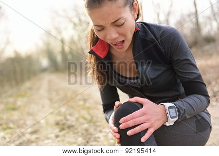 Sport and fitness injury - Female runner with hurting knee. Running woman screaming in pain during run wearing a smartwatch. Painful joint during workout.