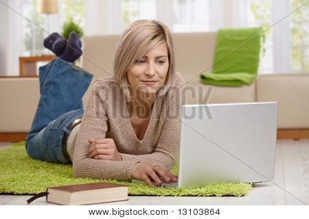 Attractive young at home in living room browsing internet on laptop computer, smiling.