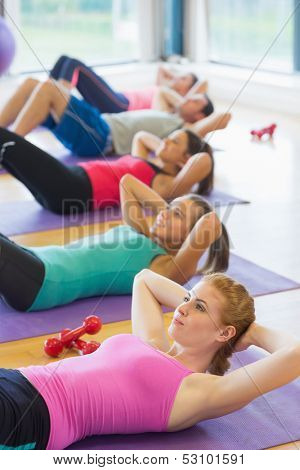 Side view of sporty fitness class doing sit ups on exercise mats