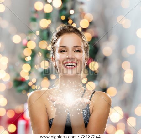 people, holidays and magic concept - laughing woman in evening dress holding something over christmas tree and lights background