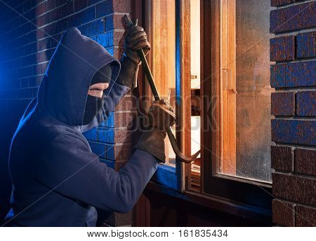 Hooded burglar breaking into a home with a crowbar