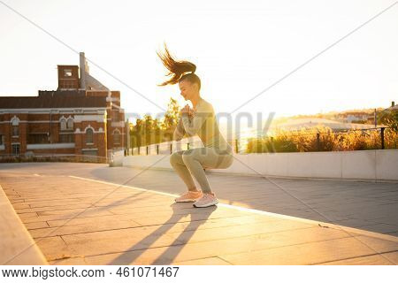 Sporty Woman Doing Jumping Squats Exercises On Stairs In Park. Bodyweight Training On Sunset. Young 