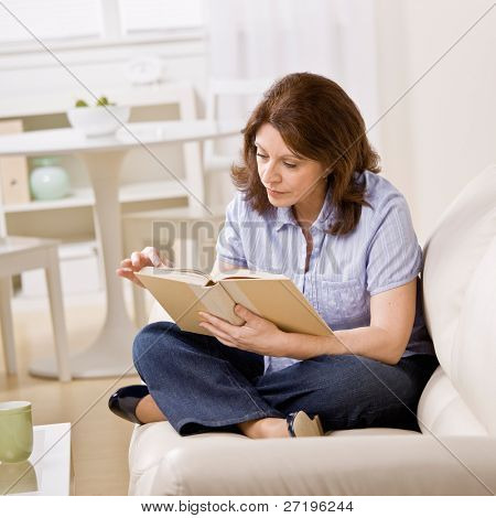 Ontspannen vrouw zitten op de Bank in de woonkamer genieten van het lezen van boek