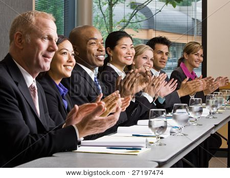 Multietniche collaboratori seduti in fila, applaudendo al tavolo conferenza