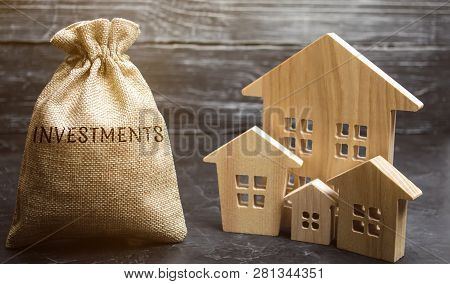 Money Bag With The Word Investments And Wooden Houses. The Concept Of Attracting Investment In Real 