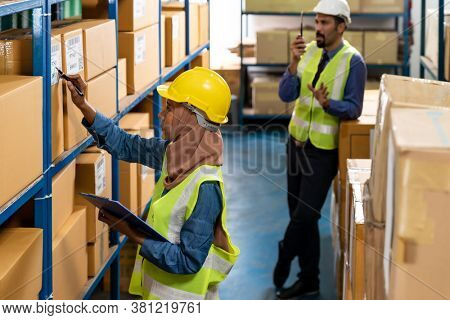 Islam Muslim female warehouse worker do logistic inventory route with his manager use walky talky inbackground in warehouse distribution. For business warehouse inventory and logistic concept.