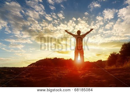 Silhouette of a man with hands raised in the sunset concept for religion, worship, prayer and praise