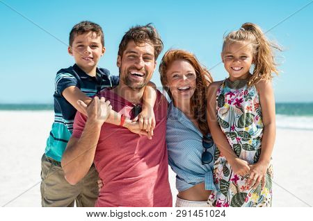 Portrait of happy family looking at camera at beach. Cheerful mother and father with cute daughter and son at sea during weekend. Smiling family with two children enjoying vacation at beach.