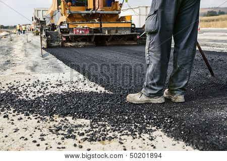 Worker operating asphalt paver machine during road construction and repairing works