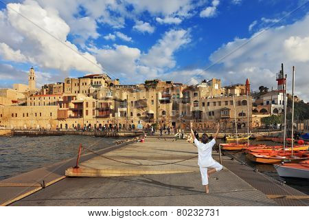 Sunset over the Old Jaffa in Tel Aviv. Fishing jetty port,  the woman in white performs asana 