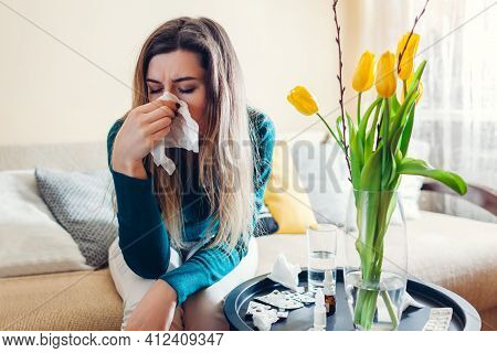 Spring Allergy. Woman Sneezing Because Of Tulips Flowers Surrounded With Pills And Nasal Drops At Ho