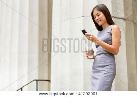 Attorney - young asian woman lawyer looking at mobile smartphone and drinking coffee from disposable paper cup. Young multiethnic female professional in the city in front of courthouse.