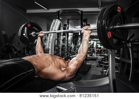 Brutal athletic man pumping up muscles on bench press