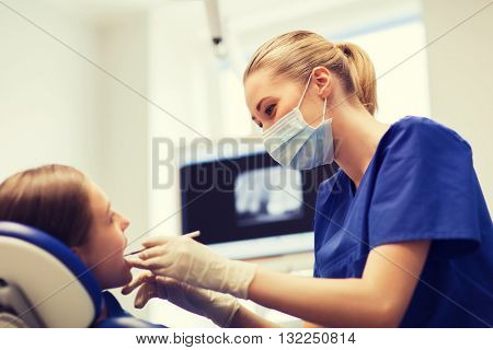 people, medicine, stomatology and health care concept - happy female dentist with mirror or dental probe checking patient girl teeth up at dental clinic office