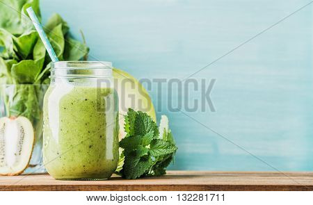 Freshly blended green fruit smoothie in glass jar with straw. Turquoise blue background, copy space