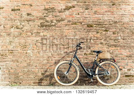 Black retro vintage bicycle with old brick wall and copy space. Retro bicycle with basket in front of the old brick wall. Old photo effect applied. Toned.