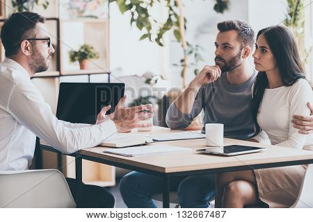 They need an expert advice. Young couple sitting together at the desk and listening to their financial advisor