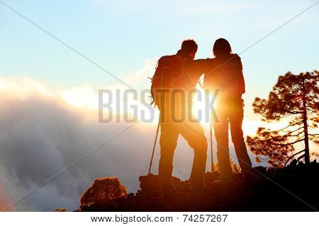 Hiking adventure healthy outdoors people standing talking. Couple enjoying sunset view above the clouds on trek. Video of young woman and man in nature wearing hiking backpacks and sticks.