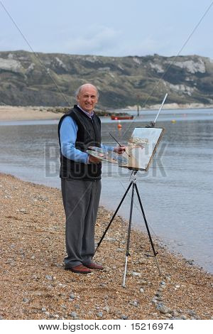 Mature artist painting a coastal landscape with paintbrush, easel and painter's palette.