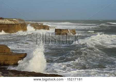 Winter storm in Portland Dorset with waves breaking against the coastline and a boat winch in the distance.