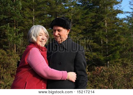 Senior couple embrace while enjoying a winter walk through a pine forest.