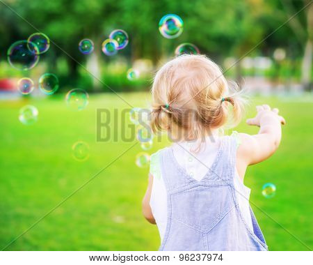 Little baby girl try to catch soap bubbles, having fun outdoors, playing games in the park, happy carefree childhood