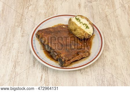 Rack Of Ribs In Barbecue Sauce Garnished With Roasted Potato With Skin And Butter And Parsley On Top