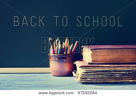 some pencils in a pot, some old books on a blue school desk, and the text back to school written on a chalkboard, with a filter effect