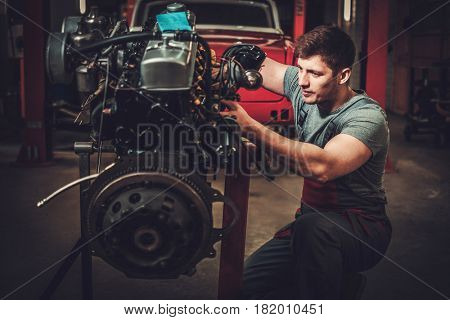 Mechanic working on classic car engine in restoration workshop