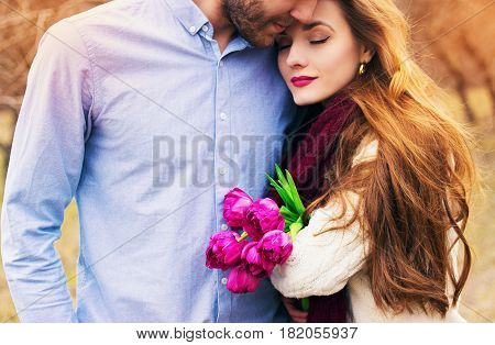 Romantic Love Story. Close-up Portrait Of Bearded Man Hugging His Lovely Girlfriend Holding Flowers.