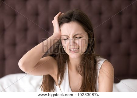 Young woman suffering from headache or migraine after wake up in morning. Stressed lady in bed with painful face expression feels terrible hangover, sharp pain in head, unpleasant weakness, dizziness