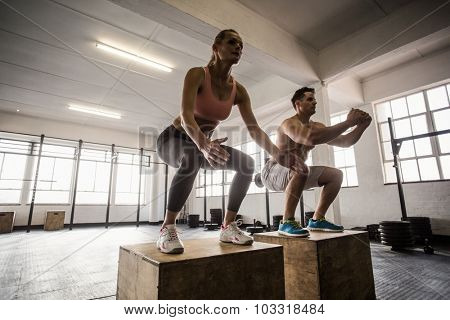 Muscular couple doing jumping squats in fit gym