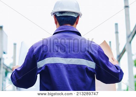 Engineer with white safety helmet holding project plan at construction outdoor site background, industrial concept