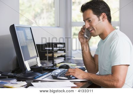 Man In Home Office On Telephone Using Computer And Smiling