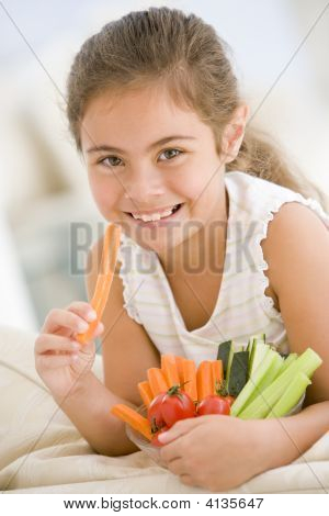 Young Girl Eating Bowl Of Vegetables In Living Room Smiling