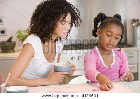 Mulher e menina na cozinha com projeto arte sorrindo