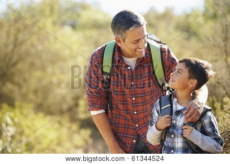 Father And Son Hiking In Countryside Wearing Backpacks