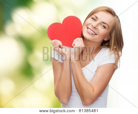 happiness, health, people, holidays and love concept - smiling young woman in white t-shirt holding red heart over green background