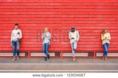 Group of multiracial fashion friends using smartphone with red wood background - Technology addiction in urban lifestyle with disinterest towards each other - Addicted people to modern mobile phones