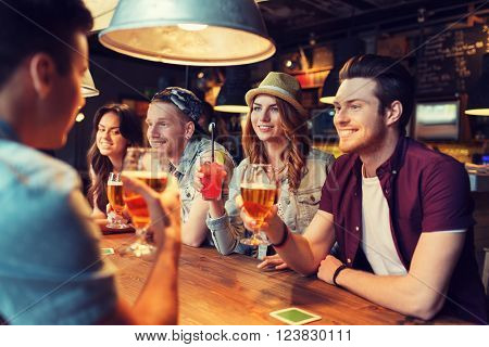 people, leisure, friendship and communication concept - group of happy smiling friends drinking beer and cocktails talking at bar or pub