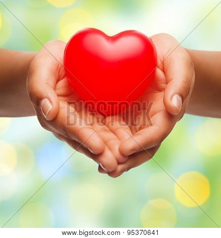 health, medicine, love, valentines day and charity concept - close up of african american female hands holding small red heart over green lights background