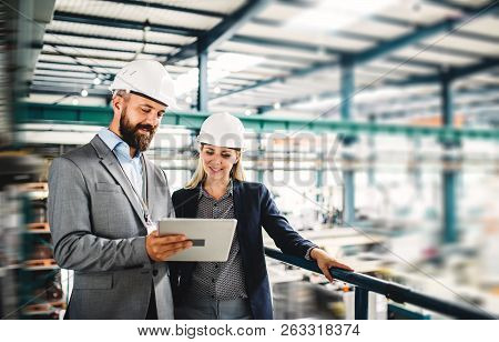 A Portrait Of An Industrial Man And Woman Engineer With Tablet In A Factory, Working.