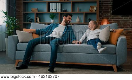 Happy Caucasian Young Family Daddy And Child Daughter Jumping On Soft Couch For Daytime Break Relaxa