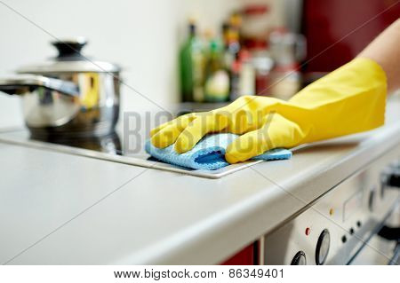 people, housework and housekeeping concept - close up of woman hand in protective glove with rag cleaning cooker at home kitchen