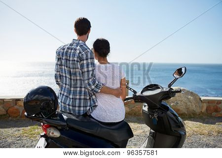 rear shot of a loving couple sitting on a scooter and enjoying the ocean view